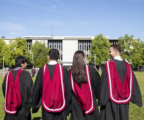 A group of 4 graduates with their backs turned to the camera.